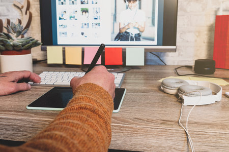 Young hipster photographer using digital graphic tablet while working in modern office, professional retoucher sitting at modern workspace with wooden table, generic design tabletの写真素材