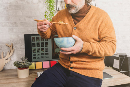 Close-up of freelancer eating oriental food, holding rice with chopsticks, resting at office desk, worker enjoying asian food at workplace during lunch.の写真素材