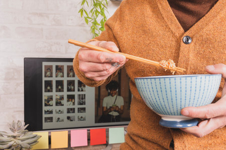 Close up of man enjoying chinese food at lunch break in office, employee holding chopsticks eating takeaway food at workplace in his office.の写真素材
