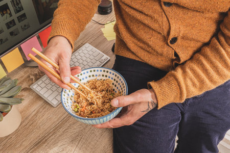 Top view of man eating on working hours, employee holding chopsticks eating takeaway food at workplace in his office.の写真素材
