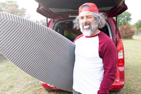 Attractive bearded hipster surfer looking at camera holding a board. Outdoor sport adventure lifestyle.の写真素材