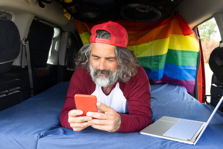 Travel photographer viewing stories on smartphone, inside minivan - Digital nomads using mobile phone apps - Technology and alternative work conceptの写真素材