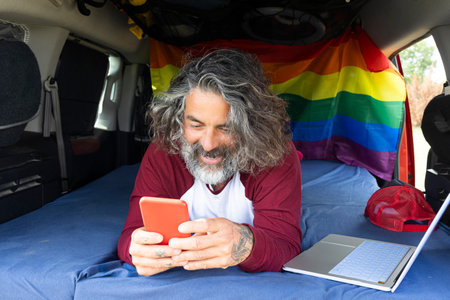 Cheerful travel photographer watching stories on smartphone, inside minivan - Digital nomads using mobile phone appsの写真素材