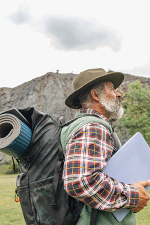 Independent male traveler with backpack mat and laptop in nature, side view.