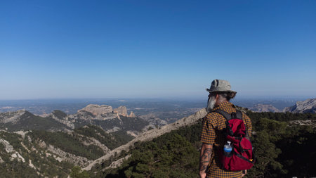 The man standing on the cliff. The hiker climbed to the rocky summit and enjoyed the views of the valley. A man looks at the clear sky in the morning sun.の写真素材
