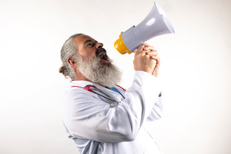 Bearded Doctor in uniform isolated on white background shouting through a megaphoneの写真素材