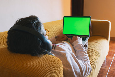 Relaxed Man Sitting On Sofa At Home Looking At Laptopの写真素材