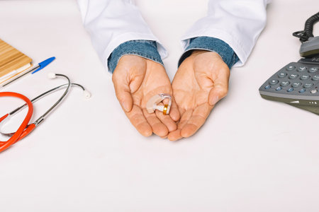Close up of the hands of an Audiologist holding a hearing aid in the palm of his hands. Conceptop audiology.の写真素材
