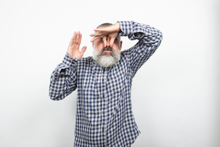 Mature man pinching his nose and covering his eyes, expressing disgust or trying to avoid a bad...