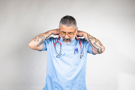 Tired doctor wearing blue uniform and stethoscope is massaging his sore neckの写真素材