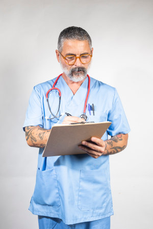 Male doctor taking notes on a clipboard, wearing scrubs and a stethoscopeの写真素材
