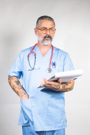 Confident doctor wearing blue scrubs, holding a patient chart, and a pen and looking asideの写真素材