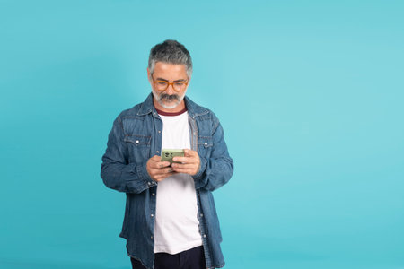 Mature man with glasses using smartphone while standing against a blue background
