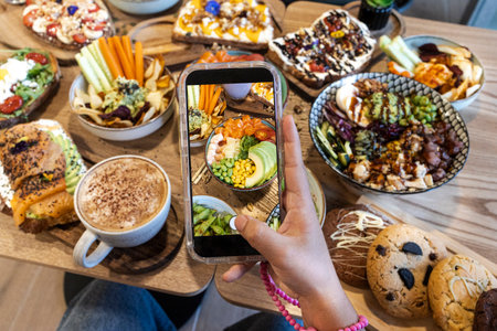 Person holding a phone, capturing an overhead view of assorted healthy food on a wooden tableの写真素材