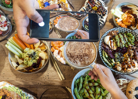 Person photographing a table filled with various healthy food bowls and a coffee drinkの写真素材