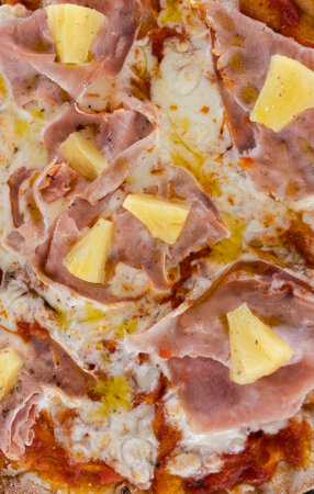 Freshly baked Hawaiian pizza showcasing melted cheese, ham, and pineapple piecesの写真素材