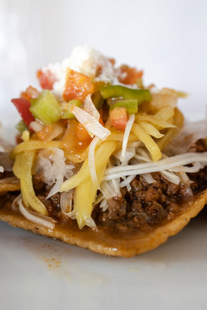Tostada with seasoned ground beef, fresh salsa, and shredded cheese on a white plate