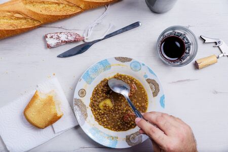 lentil soup served in a white bowl with a spoon, a knife, a piece of bread and a glass of wine.の写真素材