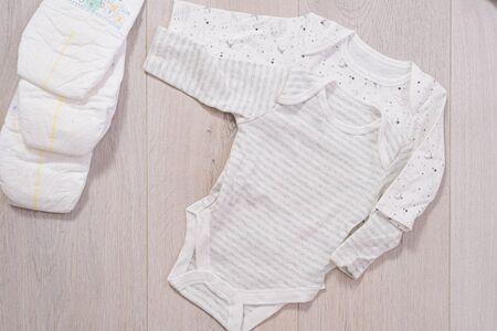 white baby clothes and diapers on wooden background. newborn