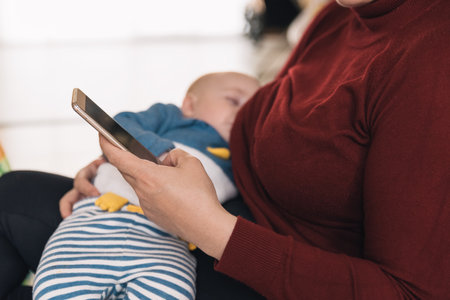 Busy single mother feeding her baby while busy with a call. The newborn baby is breastfed by its...