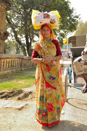 VARANASI, INDIA - FEB 9, 2014  A woman dressed in traditional sari, carrying a bag over his head 