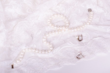 Pearl necklace and earrings on white lace cloth, wedding
