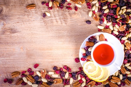Dried fruits - pecan, cranberry, raisin, almond with white cup of tea on wooden background.の写真素材
