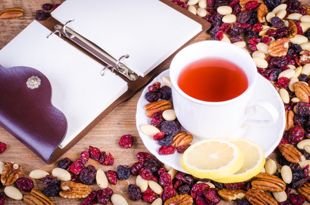 Dried fruits - pecan, cranberry, raisin, almond with white cup of tea and  open notebook on wooden background.の写真素材