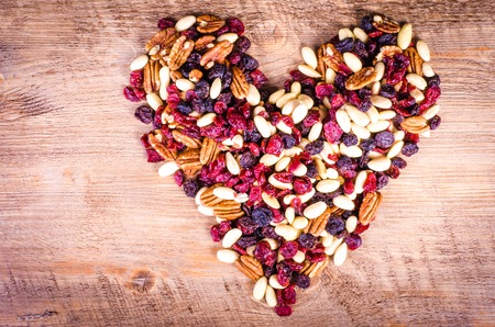 Dried fruits - pecan, cranberry, raisin, almond forming a heart on wooden backgroundの写真素材