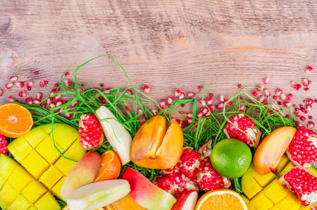 Fresh fruits on a wooden background. Raw and vegetarian eating frame. Sliced orange, persimmon, kiwi, tangerine, banana, lemon, apple,  grapefruit, pomegranate, lime, mango. Fruit set.の写真素材