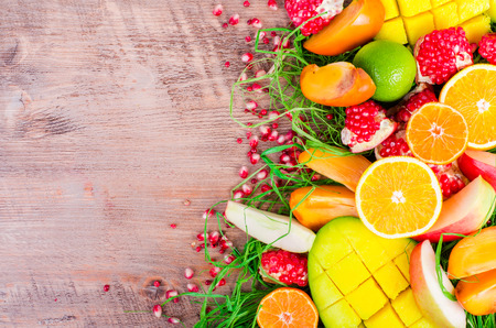 Fresh fruits on a wooden background. Raw and vegetarian eating frame. Sliced orange, persimmon, kiwi, tangerine, banana, lemon, apple,  grapefruit, pomegranate, lime, mango. Fruit set.の写真素材