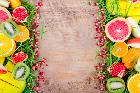 Fresh fruits on a wooden background. Raw and vegetarian eating frame. Sliced orange, persimmon, kiwi, tangerine, banana, lemon, apple,  grapefruit, pomegranate, lime, mango. Fruit set.の写真素材