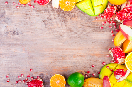 Fresh fruits on a wooden background. Raw and vegetarian eating frame. Sliced orange, persimmon, kiwi, tangerine, banana, lemon, apple,  grapefruit, pomegranate, lime, mango. Fruit set.の写真素材
