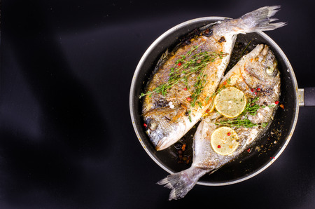 Roasted gilthead fishes with lemon, herbs, salt on black background. Healthy food concept. Food frame. Free space for your text.の写真素材