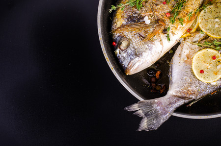 Roasted gilthead fishes with lemon, herbs, salt on black background. Healthy food concept. Food...