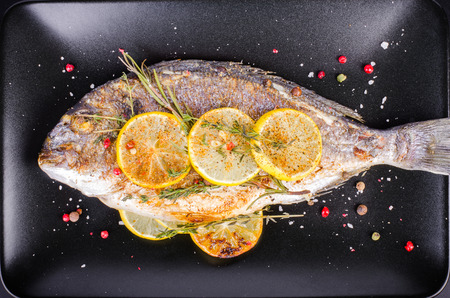 Roasted gilthead fishes with lemon, herbs, salt on black background. Healthy food concept. Food...