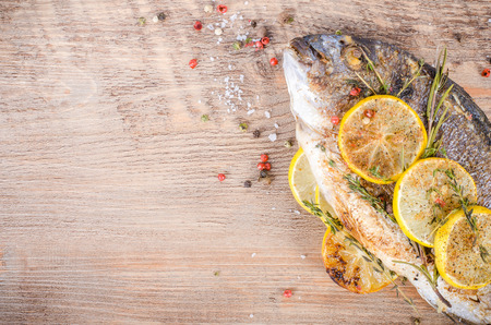 Roasted gilthead fishes with lemon, herbs, salt on wooden background. Healthy food concept. Food frame. Free space for your text.の写真素材