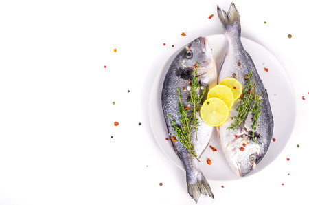 Fresh raw gilthead fishes with lemon, herbs, salt on plate, white background. Healthy food concept. Food frameの写真素材