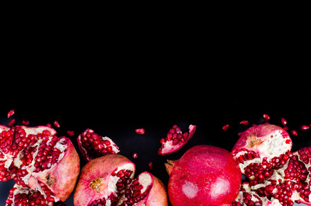 Red juicy pomegranate, whole , half, ripe and broken fruits on black background. Free space for your text.の写真素材