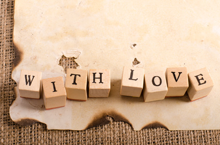 Old vintage sheet of paper and words "with love" on cubes on burlap, sackcloth background. Retro design effects.の写真素材