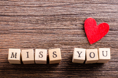 Wood cubes with inscription MISS YOU and red textile heart on wooden background. Free space for your...