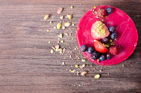 Delicious raspberry cake with fresh strawberries, raspberries, blueberry, currants and pistachios on wooden background. Free space for your text.の写真素材