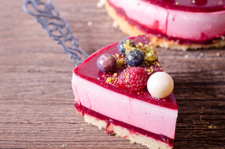 Piece of delicious raspberry cake with fresh strawberries, raspberries, blueberry, currants and pistachios on shovel, wooden background. Free space for your text.の写真素材
