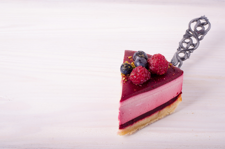 Piece of delicious raspberry cake with fresh raspberries, blueberry, currants and pistachios on shovel, white background. Free space for your text.の写真素材