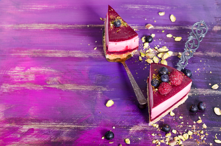 Piece of delicious raspberry cake with fresh raspberries, blueberry, currants and pistachios on shovel, bright purple, violet background. Free space for your text.の写真素材