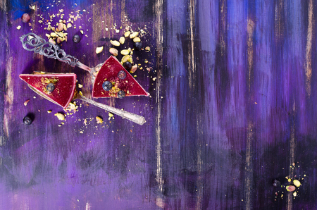 Pieces of delicious raspberry cake with fresh raspberries, blueberry, currants and pistachios on shovel, bright violet, blue background. Free space for your text.の写真素材