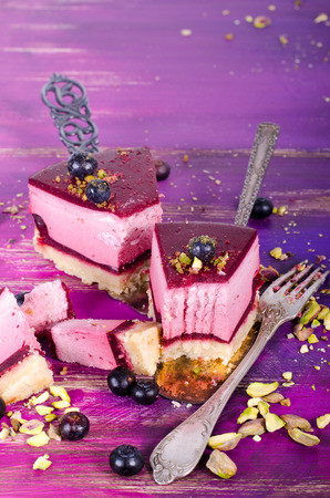 Piece of delicious raspberry cake with fresh raspberries, blueberry, currants and pistachios on shovel, bright purple, violet background. Free space for your text.の写真素材