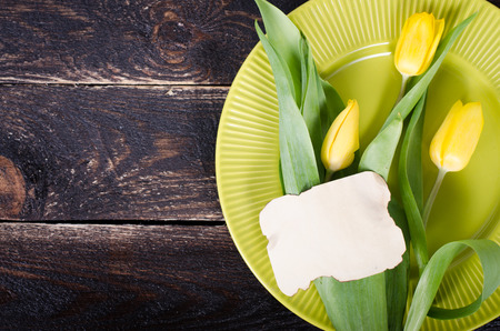 Fresh yellow tulip flowers on wooden table with green plate. Top view with copy space over wooden background.の写真素材