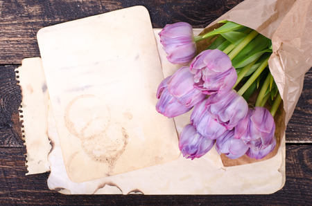 Violet tulips and vintage paper on a wooden background. Free space for your text.の写真素材