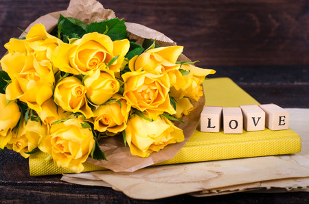Wooden cubes with inscription "LOVE" and bouquet of yellow flowers on vintage paper, wooden background. Selective focus.の写真素材